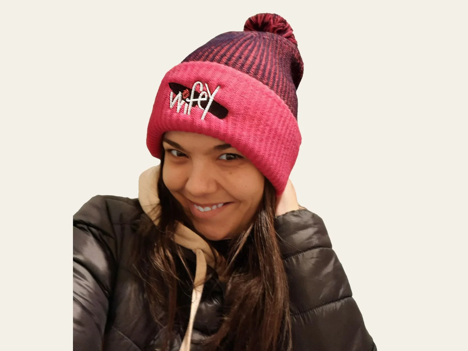 A woman smiling in a pink and maroon pom-pom toque embroidered with the Wifey submark