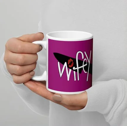 A hand holding a pink mug printed with the Wifey submark